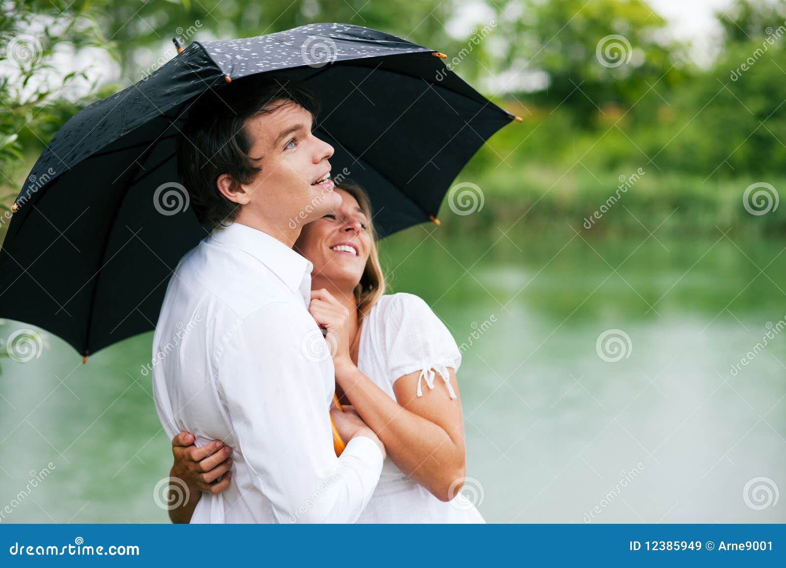 Bescherming tegen de de zomerregen. Paar (man en vrouw) bij een meer in de zomerregen met een paraplu, beschut hij haar van de dalingen, die zijn meisje in zijn wapens houden