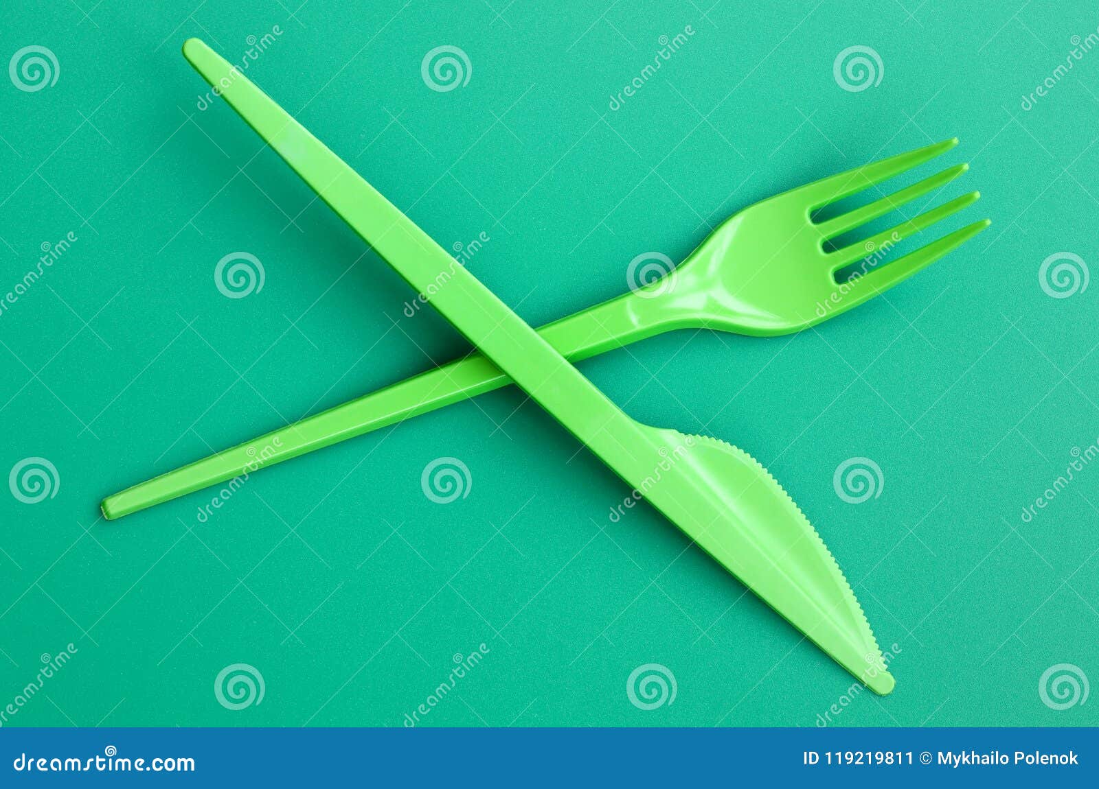 Beschikbaar plastic groen bestek De plastic vork en het mes liggen op een groene oppervlakte als achtergrond