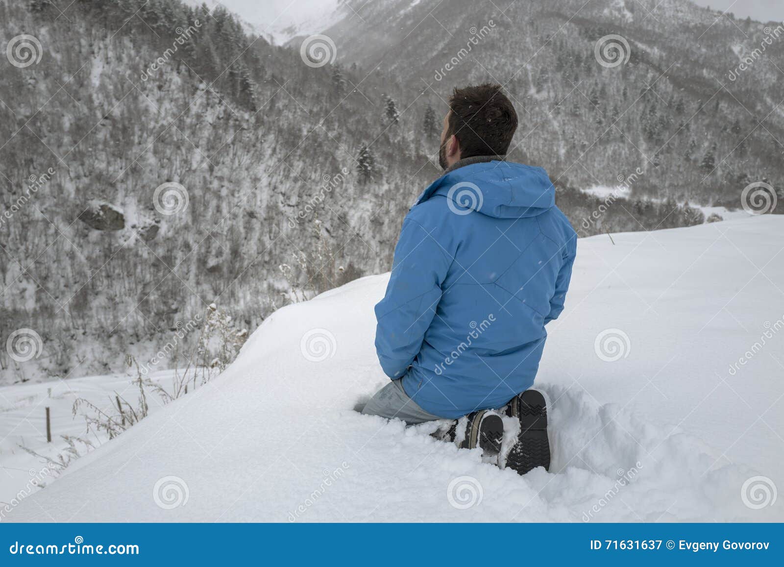 Betender Mann. Mann betet Sitzplätze im Schnee herum von Bergen