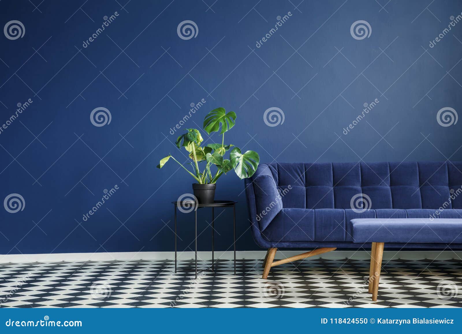 big plant on a stool next to a comfy couch and checkered tiles s