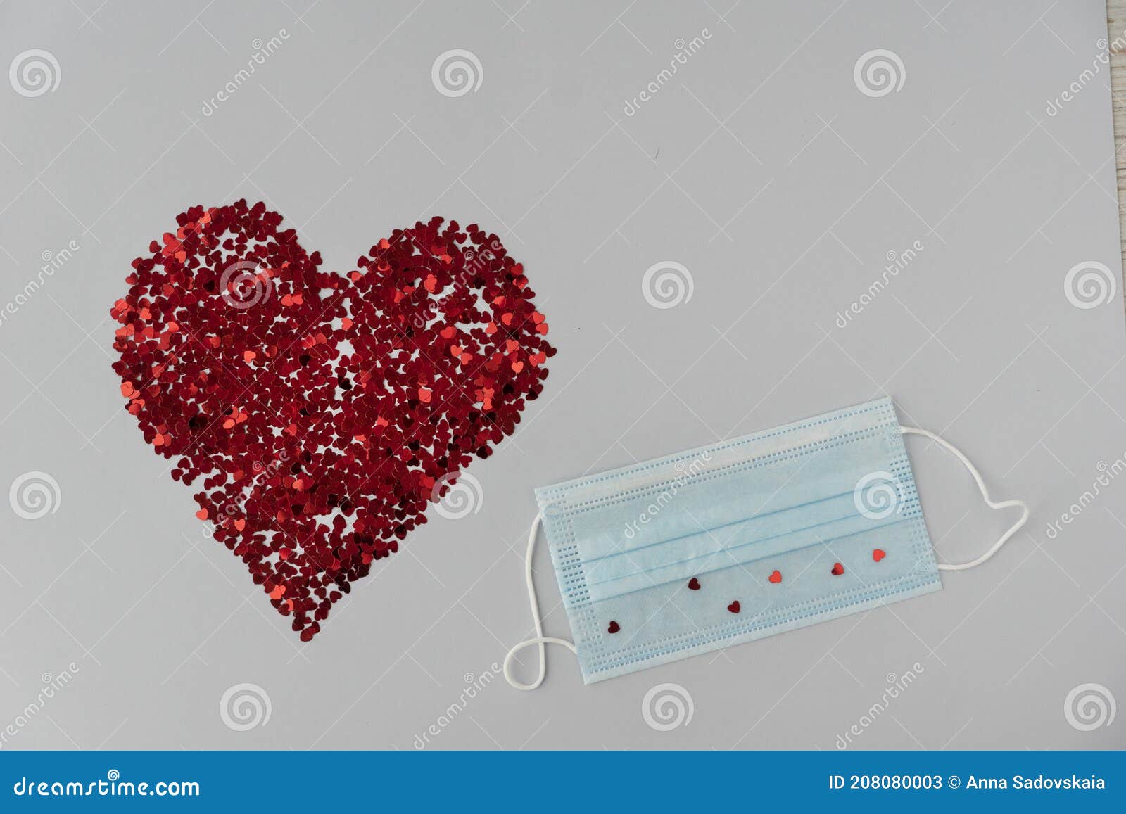 big red heart from little sparkling confeti and medical mask on light background.