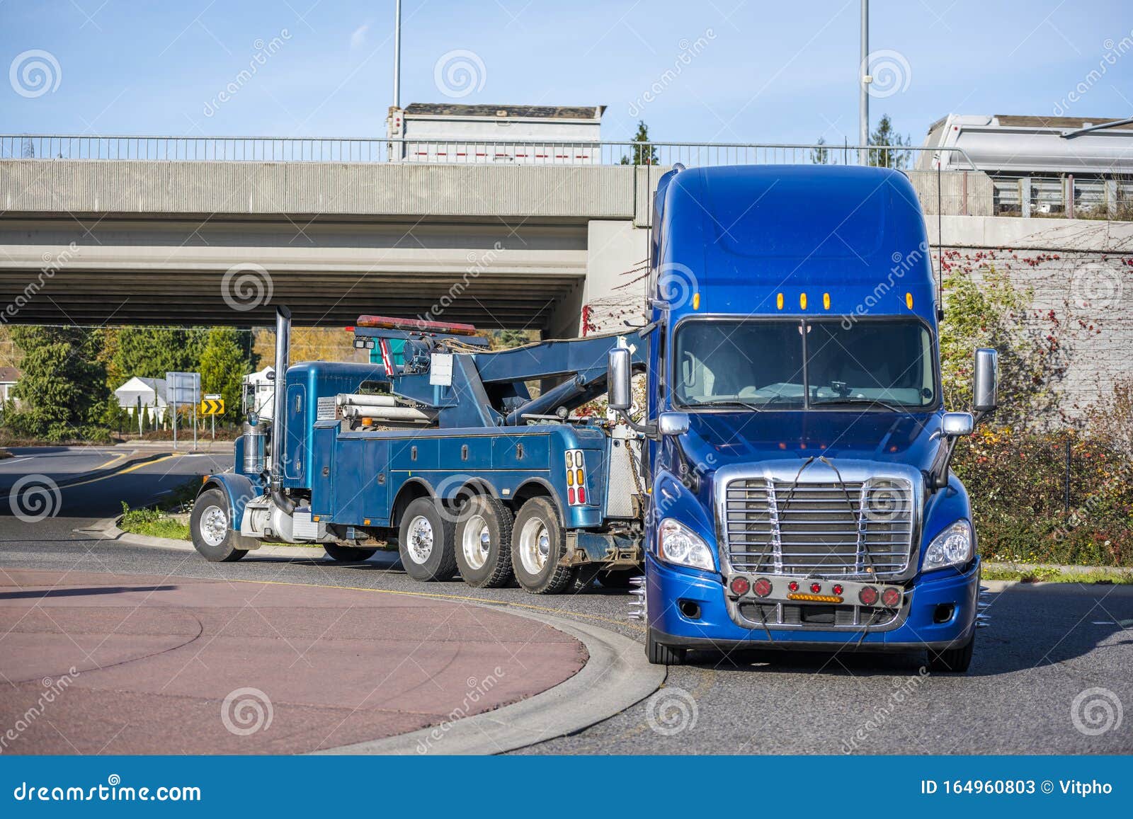 big rig tow truck towing broken blue big rig semi truck tractor going under the bridge