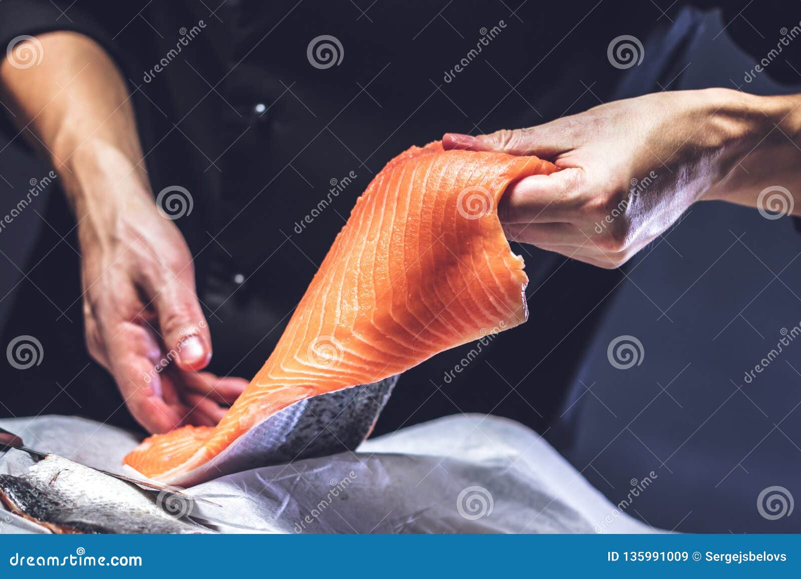 The Big Salmon is in the Hands of the Chef Cook. he is Using a Knife To