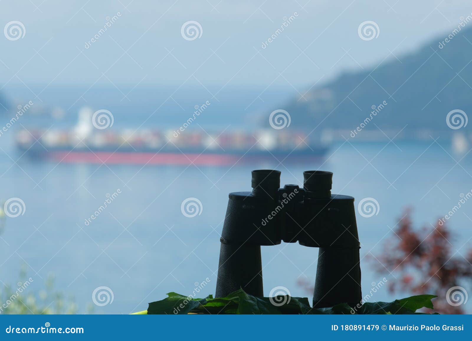 binoculars resting on a table. container ship cargo ship on the background. ligurian mediterranean sea in the gulf of la spezia