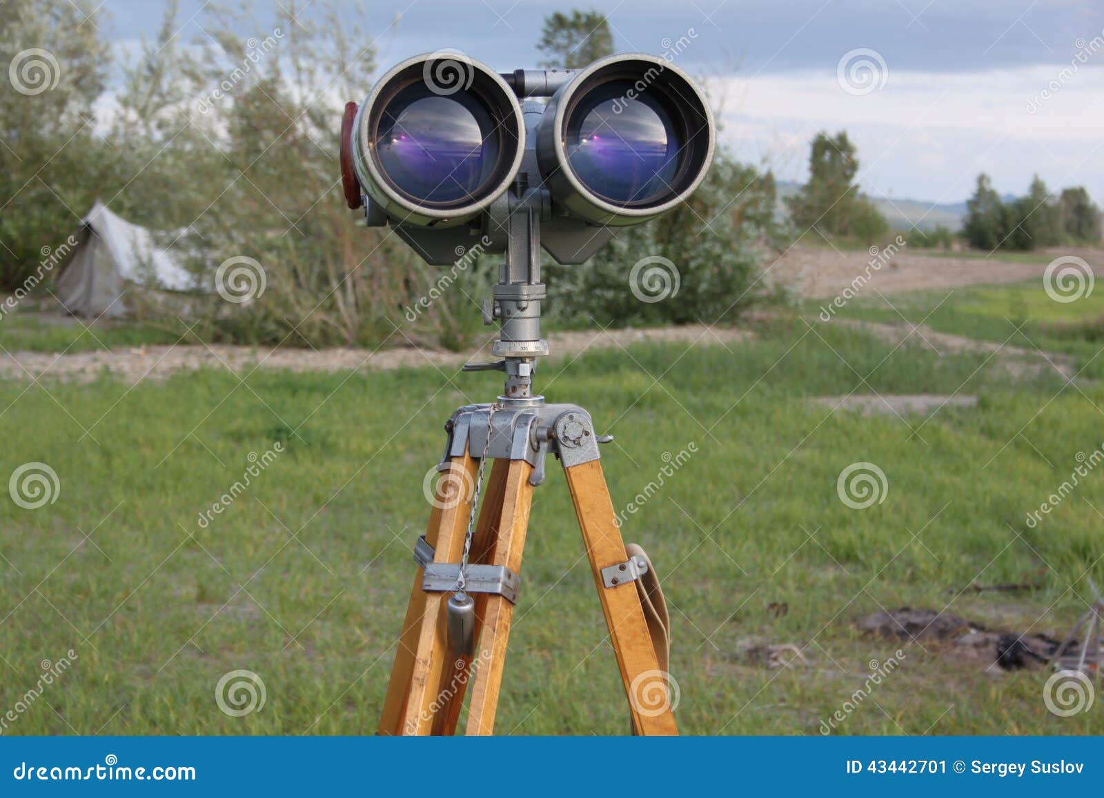 a binoculars with a tripod with a azimuth head in a forest on a sand with grass