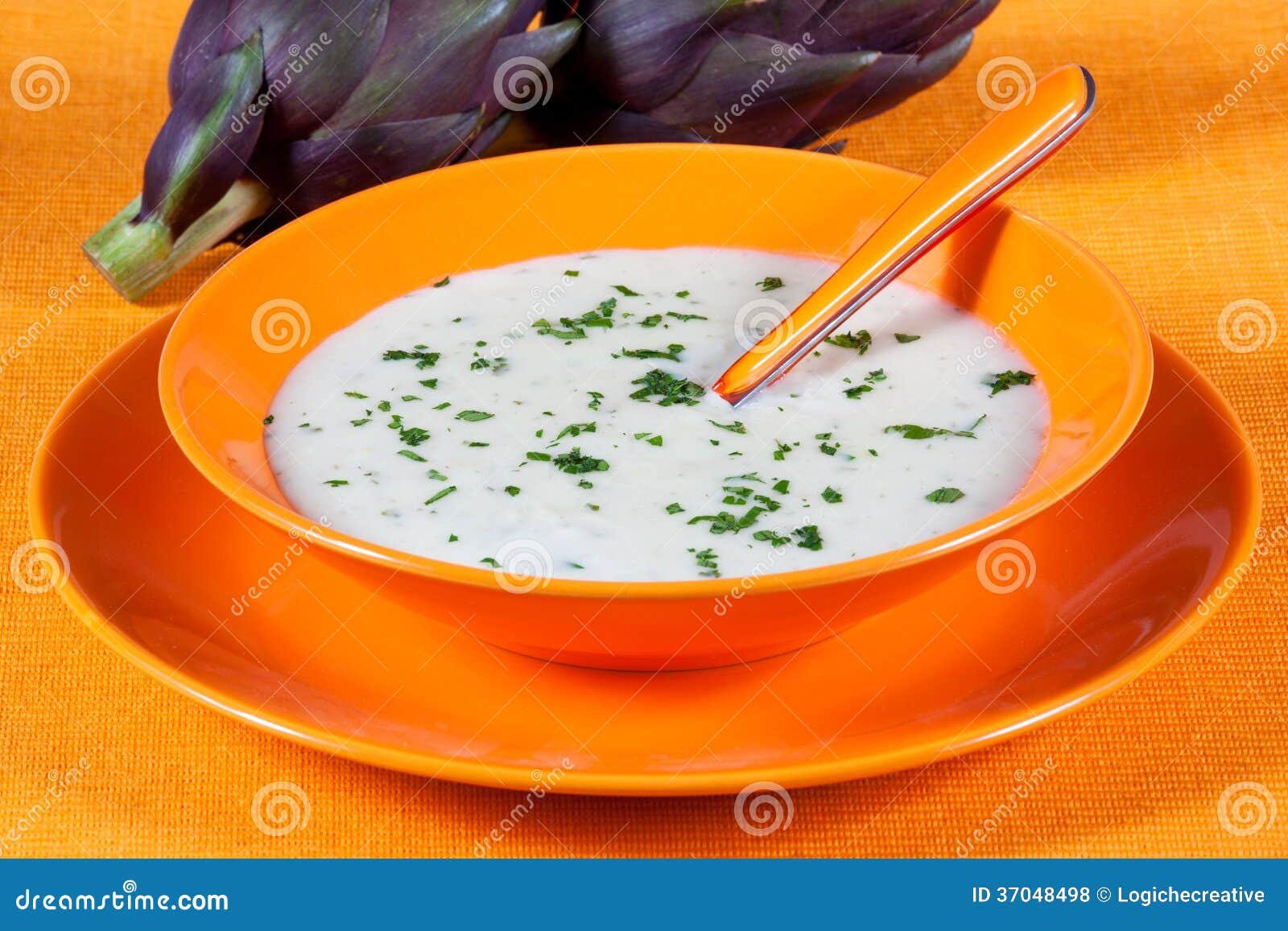 Biologische Suppe der Artischocke in einem Teller. Vegetarische Suppe der Artischocke in einem Teller auf einer orange Tabelle