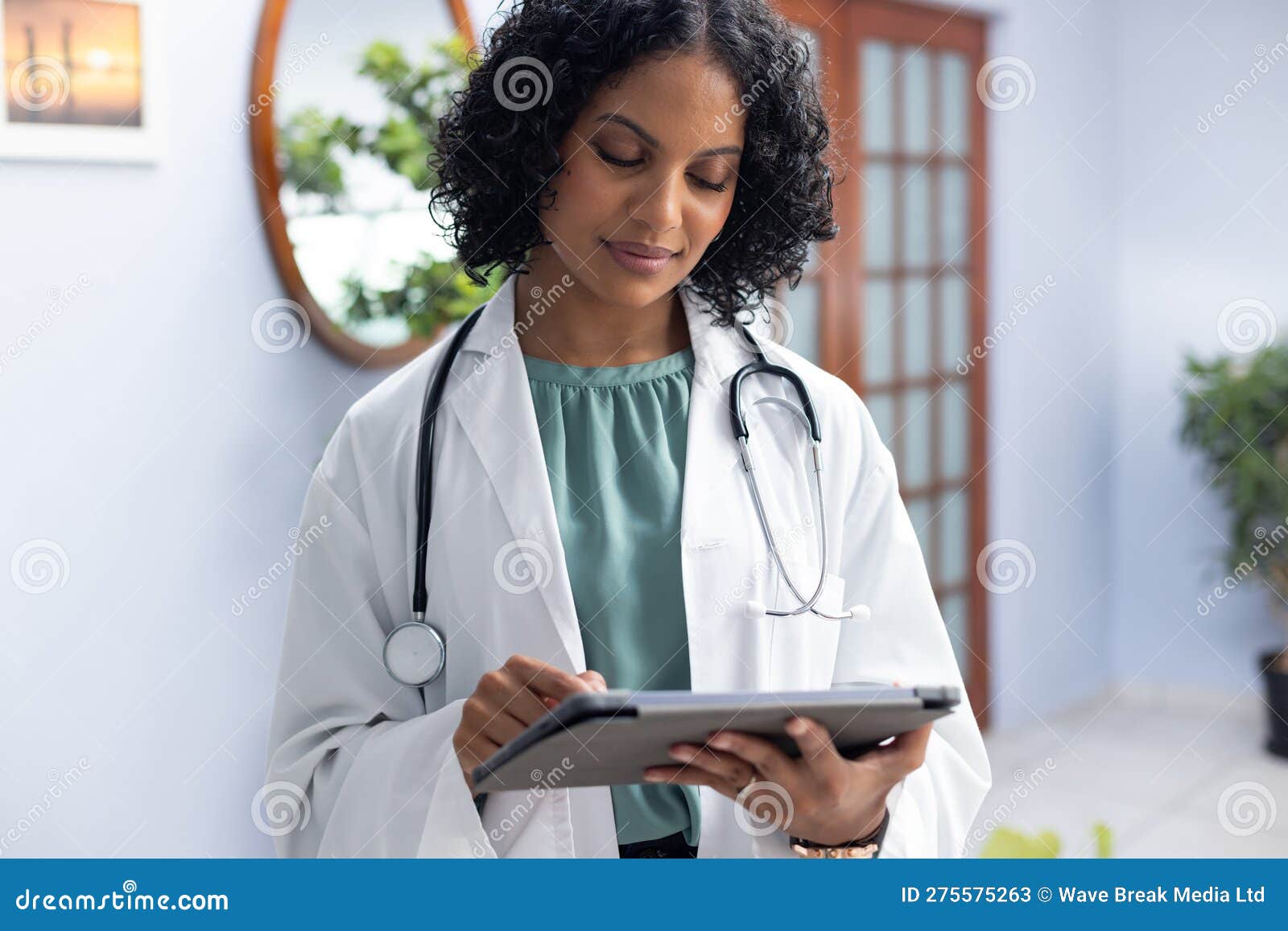 biracial female doctor wearing sthethoscope, using tablet at doctor's office