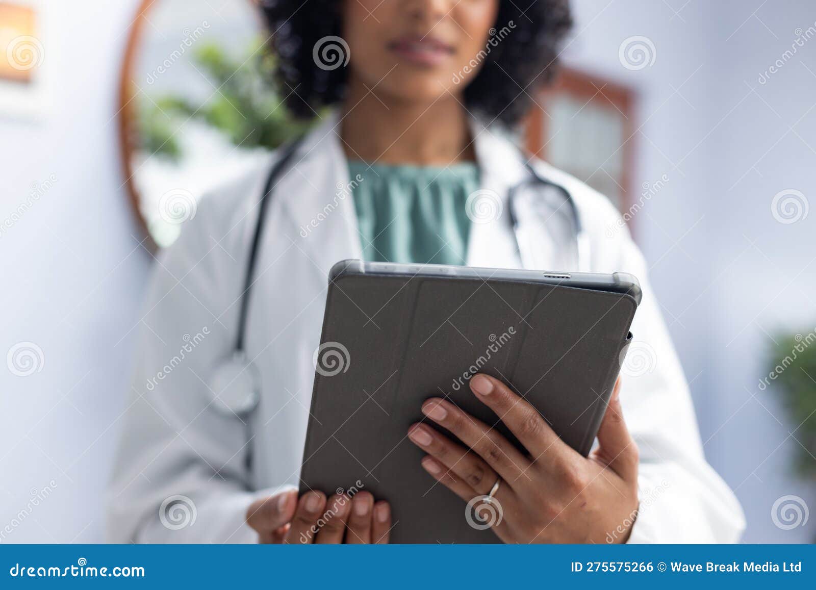 biracial female doctor wearing sthethoscope, using tablet at doctor's office