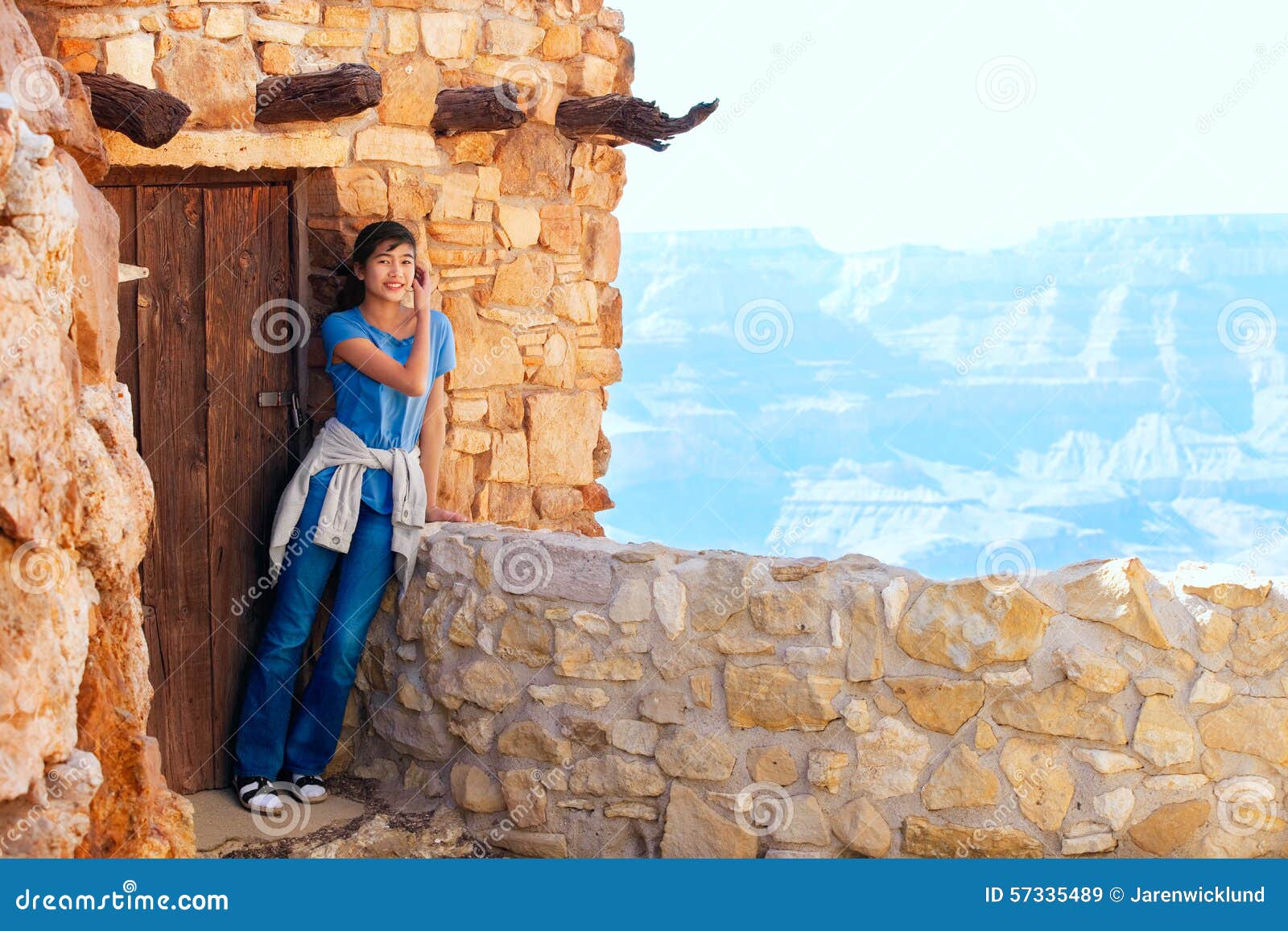 Biracial teen girl relaxing, leaning against rock wall overlooking Grand Canyon, next to doorway