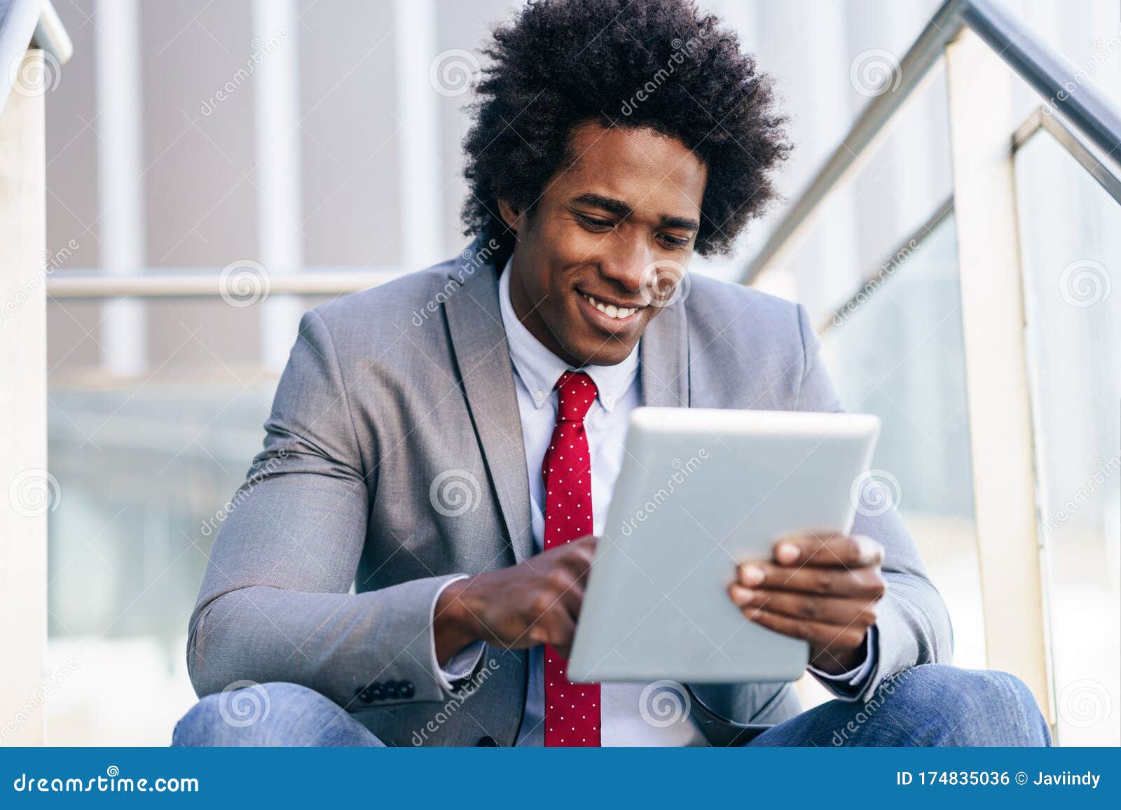 black businessman using a digital tablet sitting near an office building.