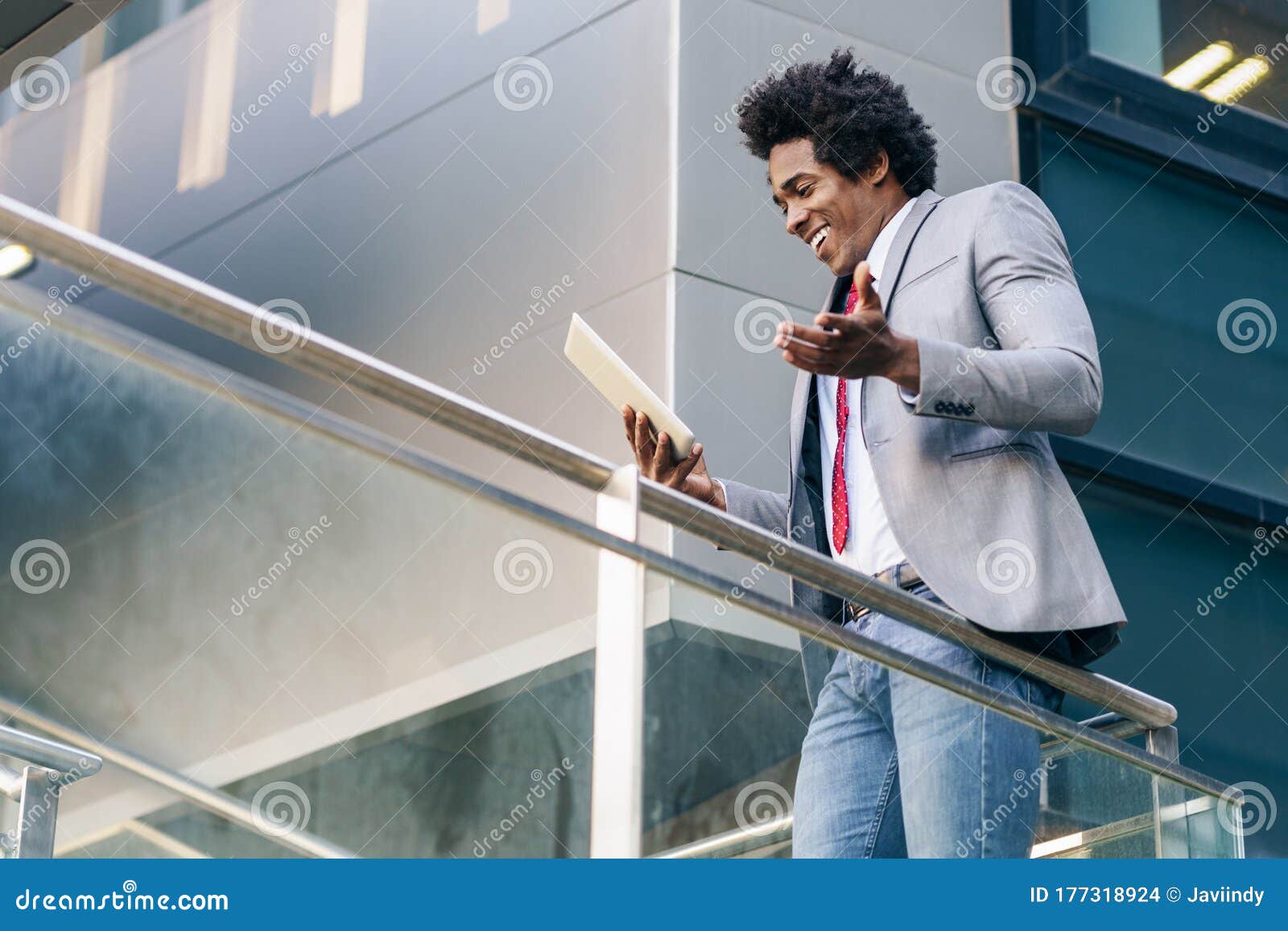 black businessman using a digital tablet sitting near an office building.