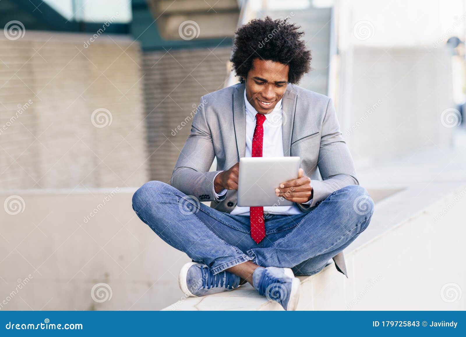 black businessman using a digital tablet sitting near an office building.