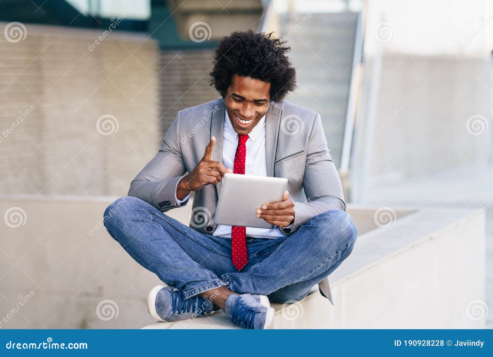 black businessman using a digital tablet sitting near an office building.