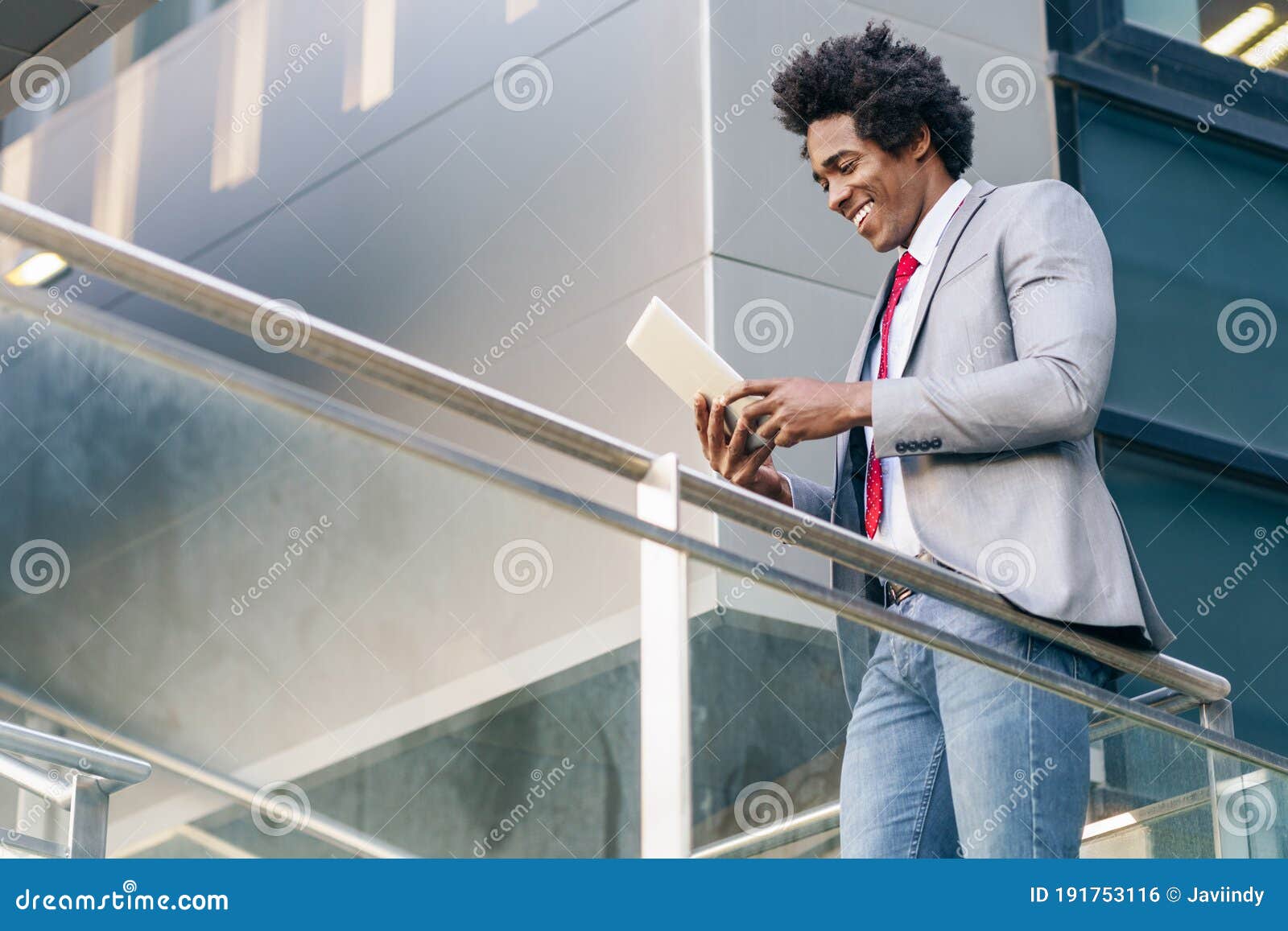 black businessman using a digital tablet sitting near an office building.