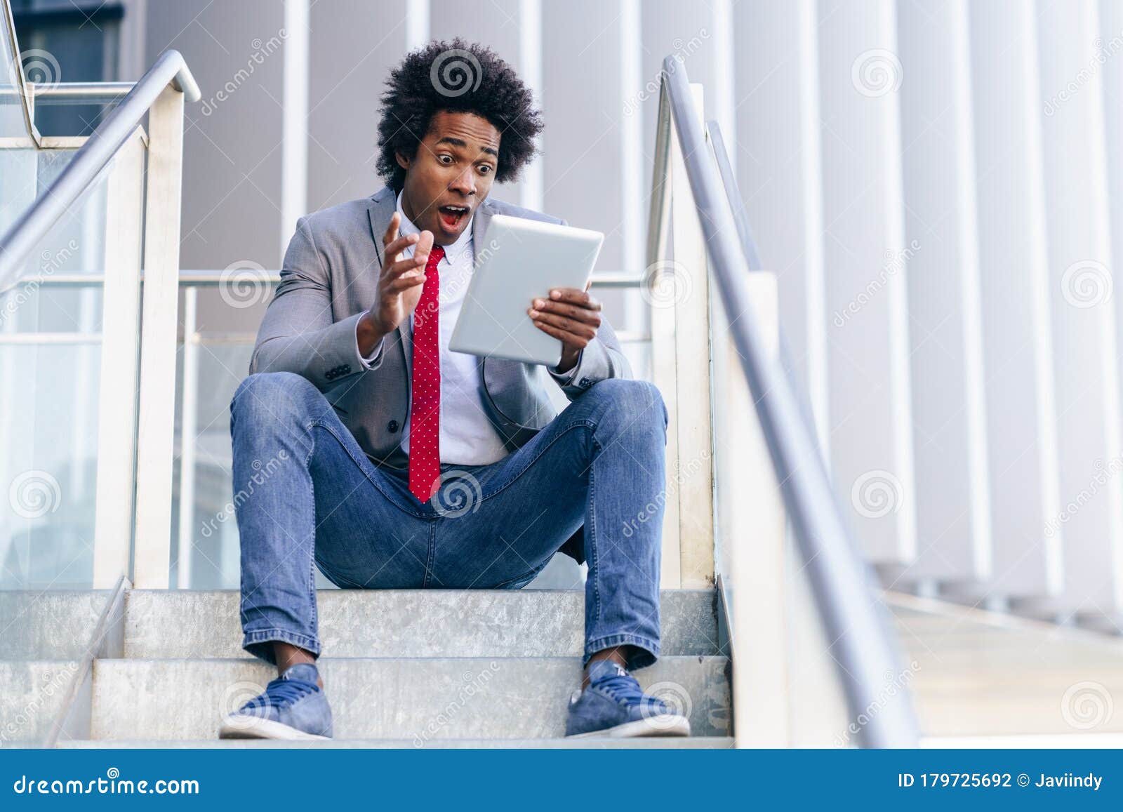 black businessman using a digital tablet sitting near an office building.