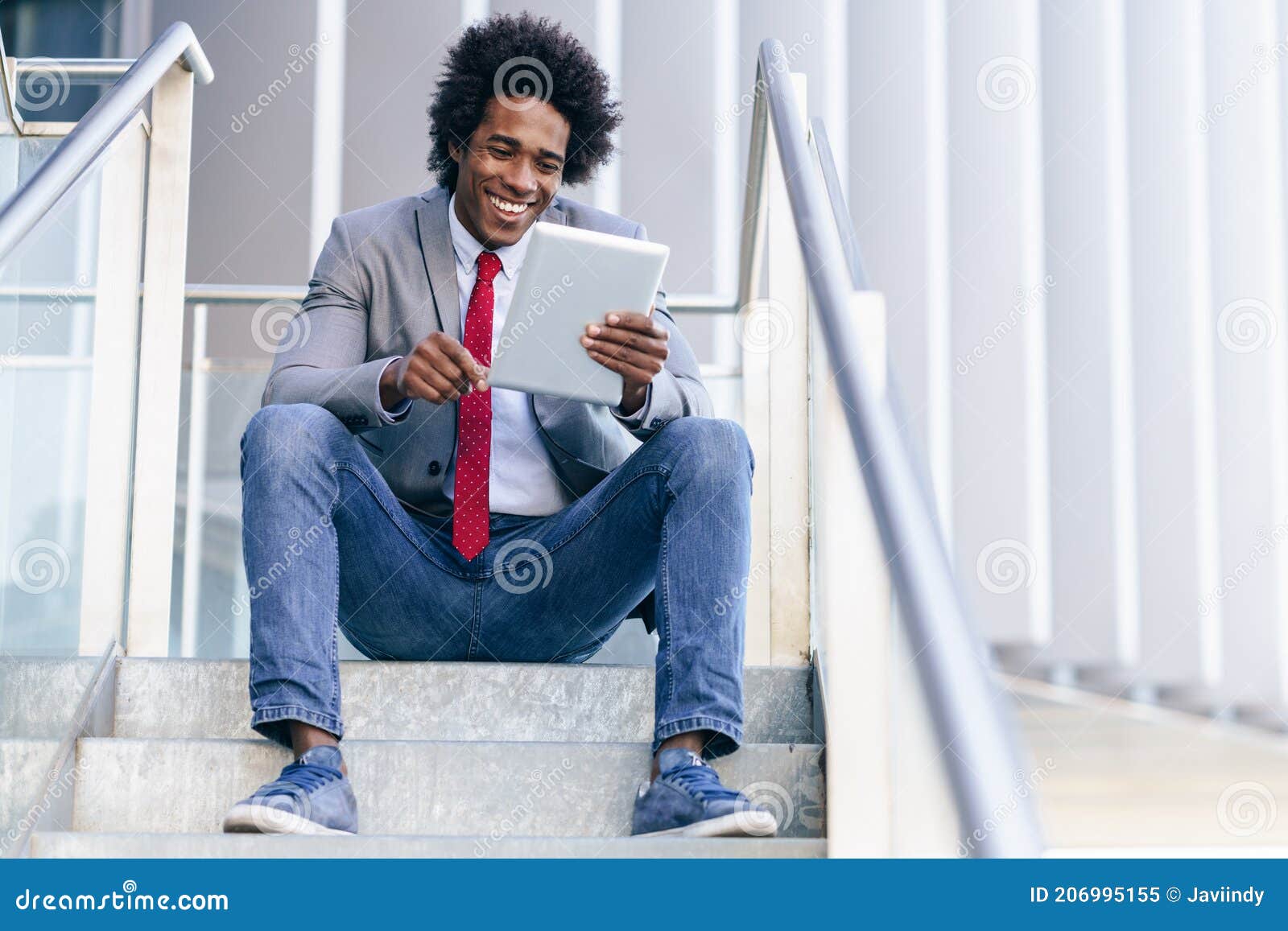 black businessman using a digital tablet sitting near an office building.