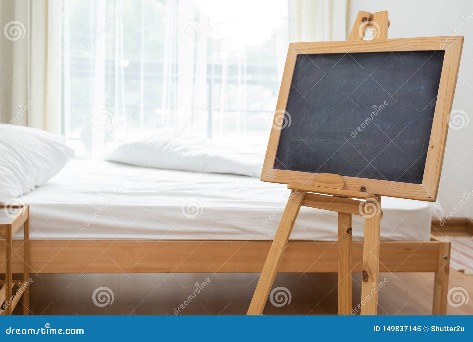 Black Chalkboard On Easel Stand In Bedroom With White Soft Bed