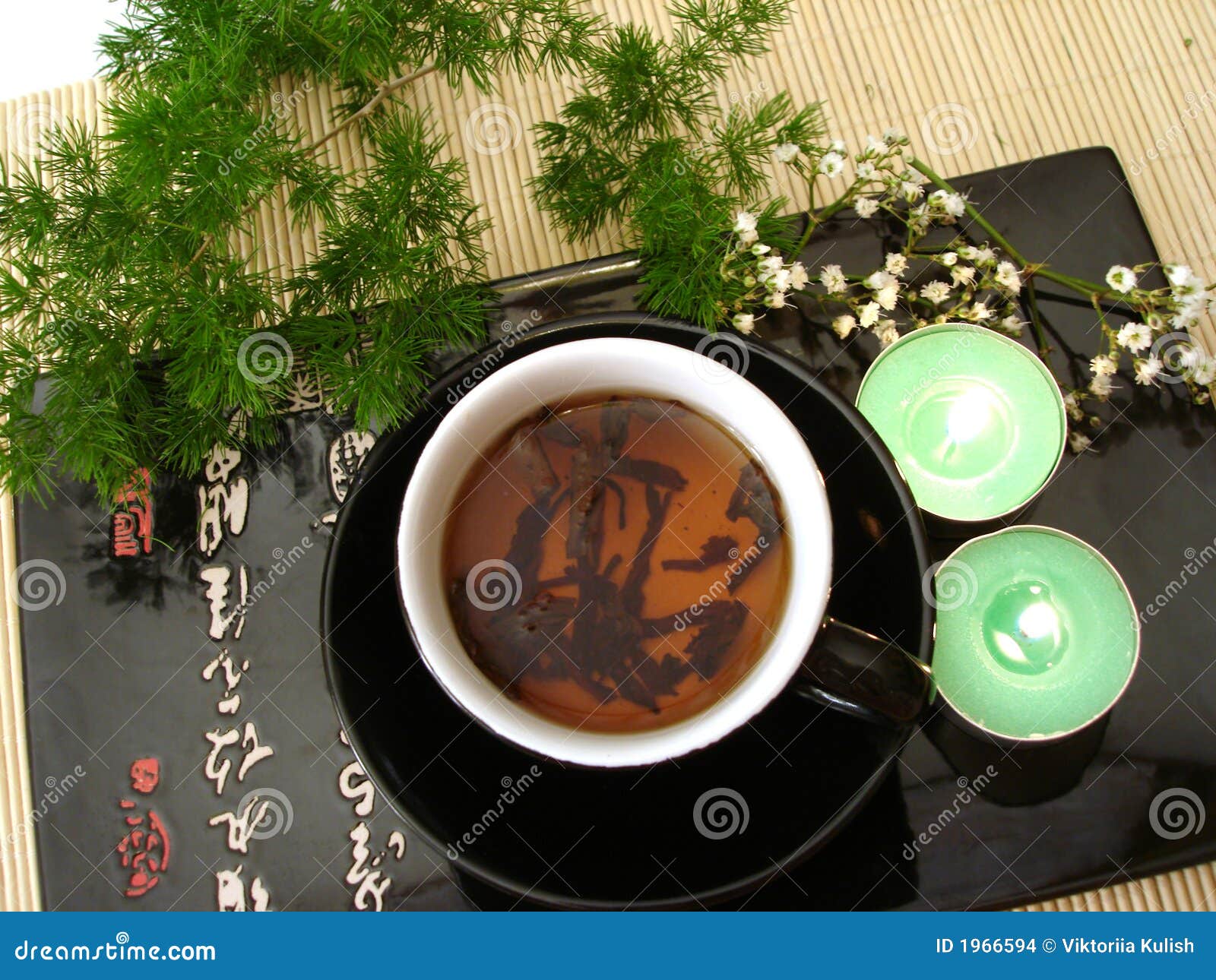 black cup of tea with green branch and candles over straw matt