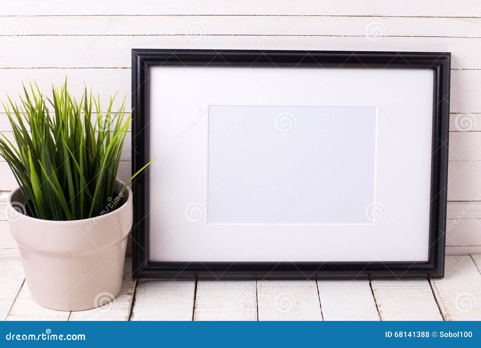 Black empty frame and grass in pot on white wooden background. Place for text. Selective focus.