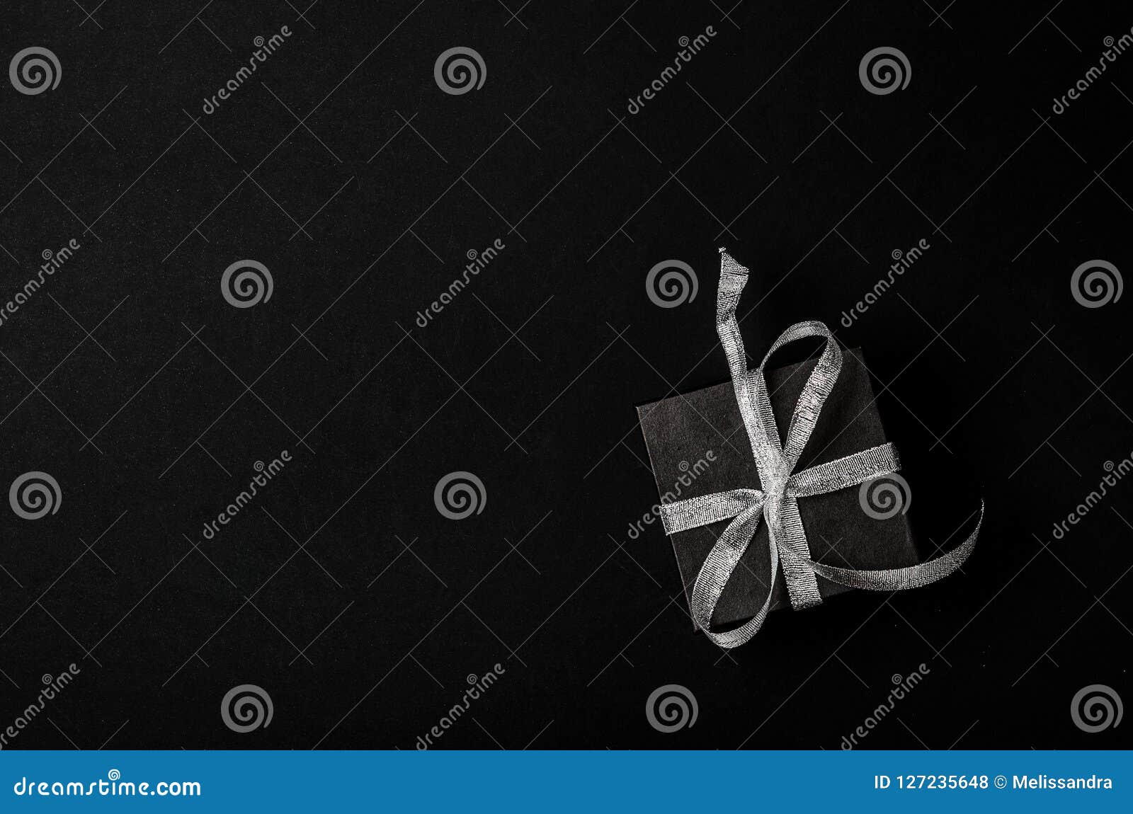 Black Gift Box with Silver Ribbon Bow on Black Background. Top View