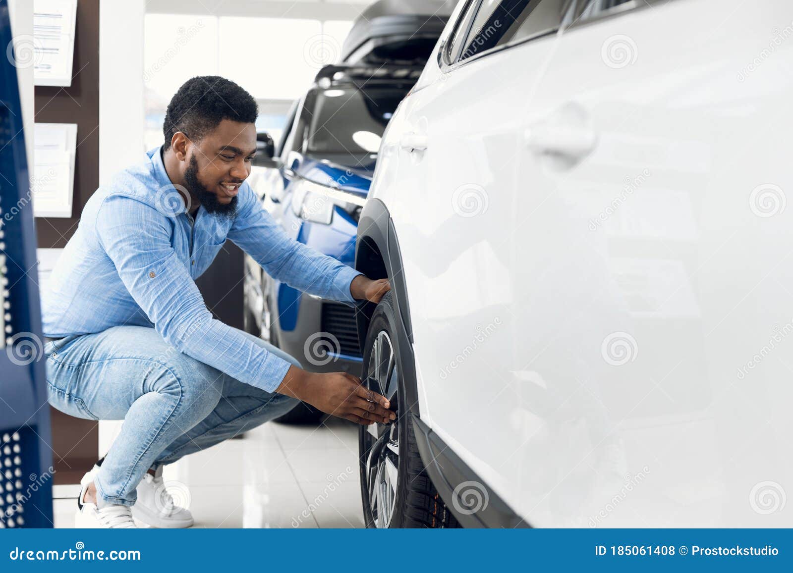 black guy checking car wheels and tyres in dealership showroom