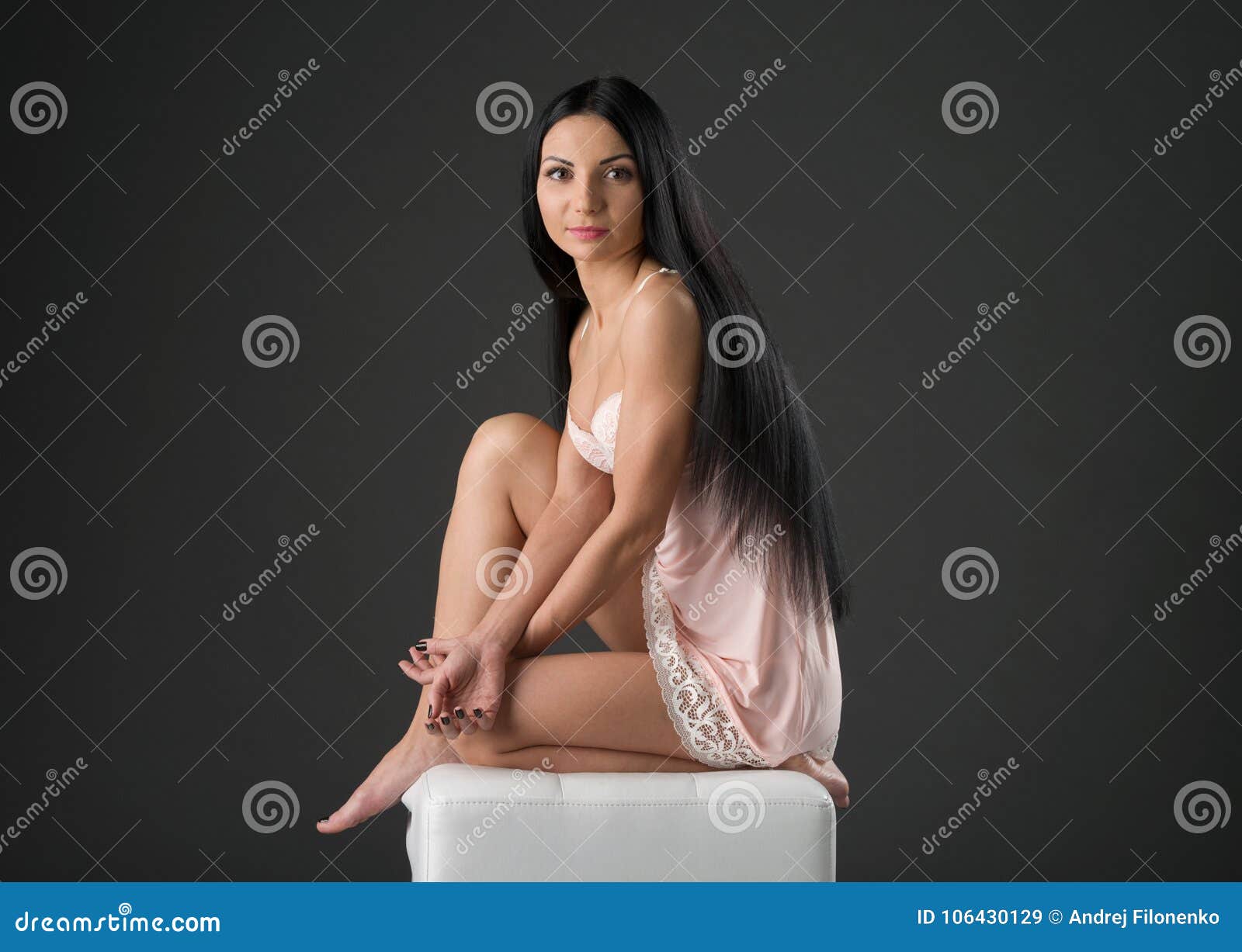 black-haired model in a pink nightie posing on top of a white puff