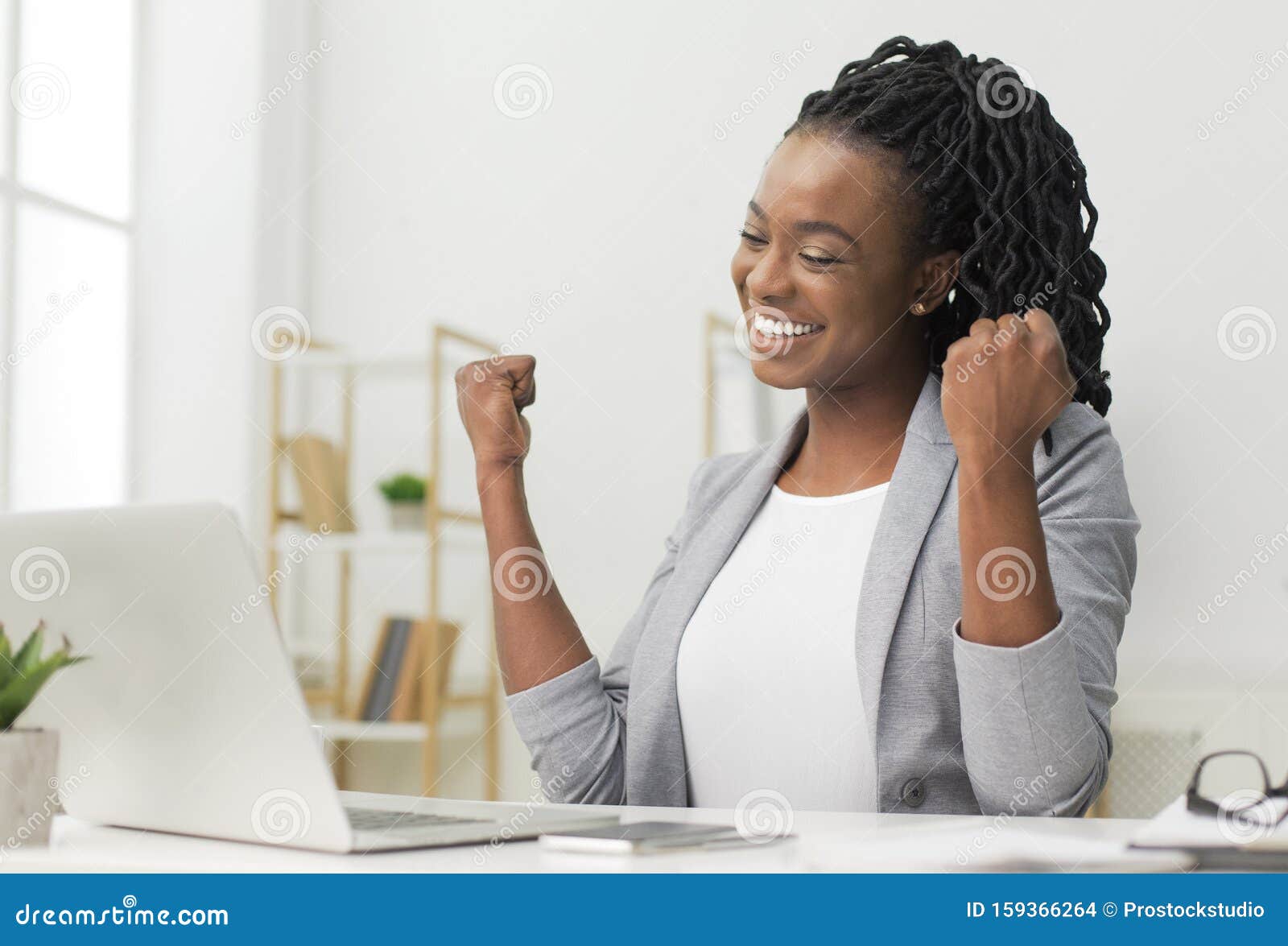 black lady celebrating business success sitting at laptop in office