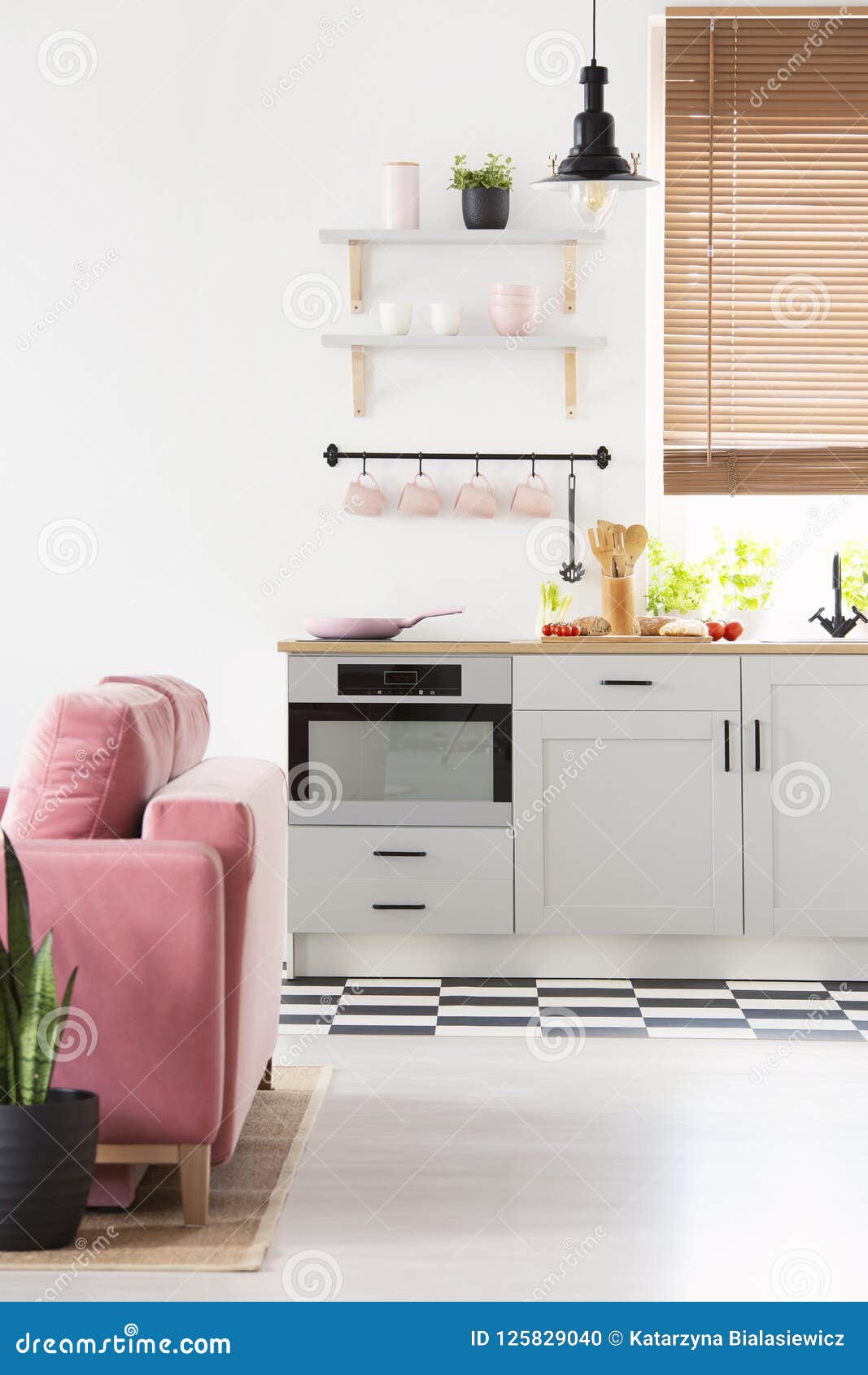 black lamp above grey kitchenette in open space interior with pink sofa and window. real photo