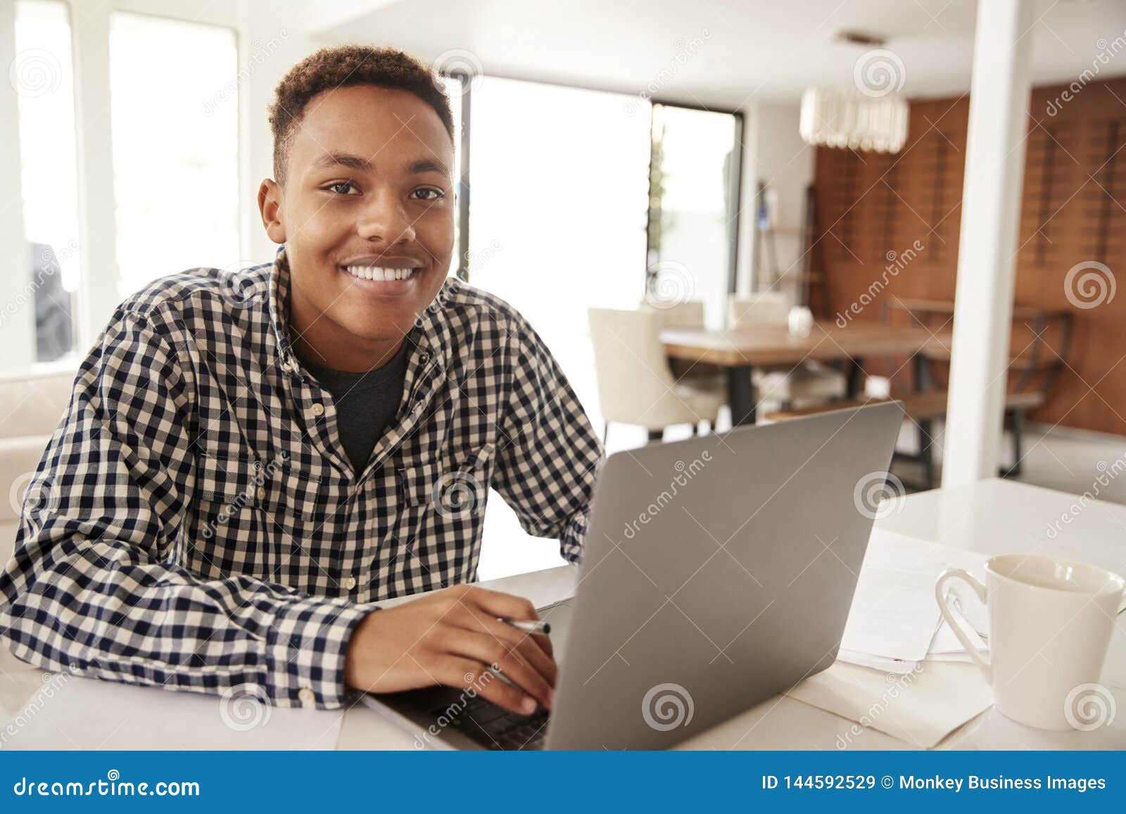 african american  male teenager using a laptop computer at home smiling to camera, close up