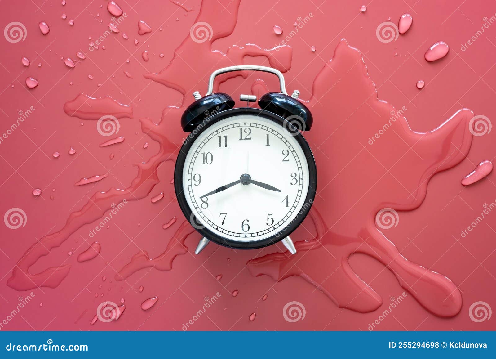 black retro alarm clock in a pool of spilled water on a red background. top view.