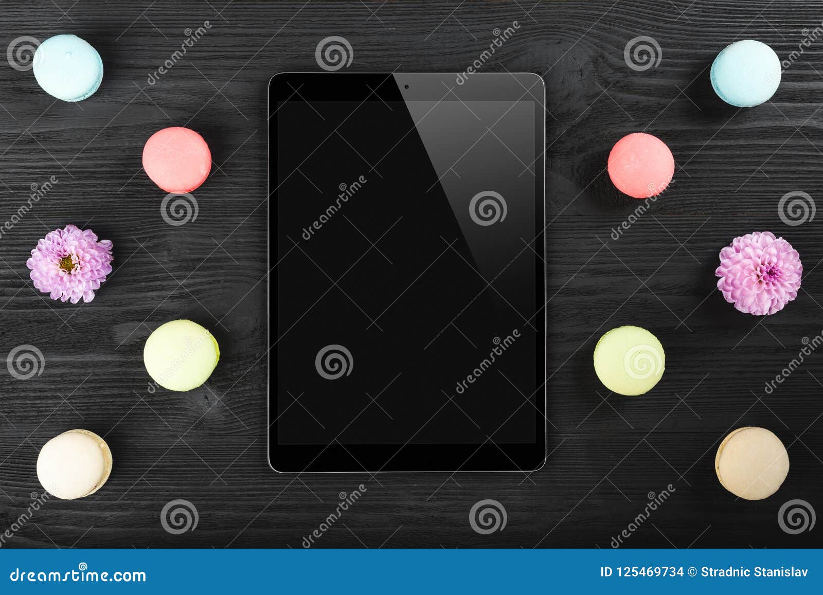 black tablet pc looking similar to ipad and colorful macarons on old dark wood background