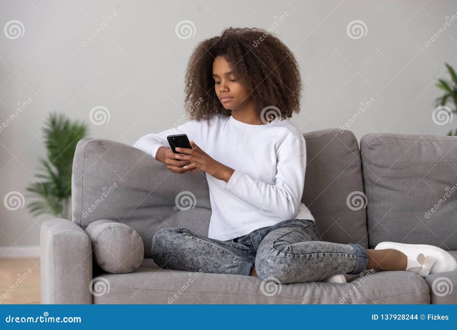 Black Teenage Girl Relax On Couch Using Smartphone Stock Photo