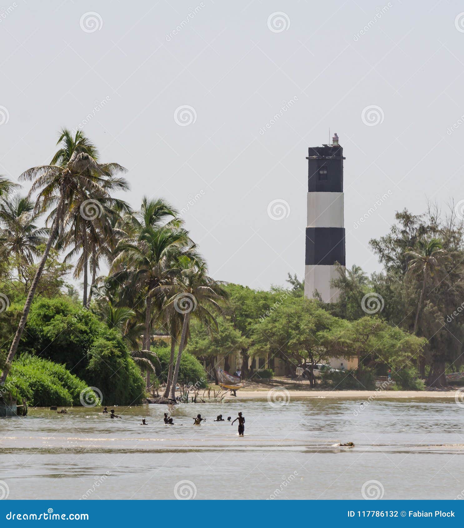 black and white lighthouse with palms, trees and swimming locals at the sea, ndiebene, senegal