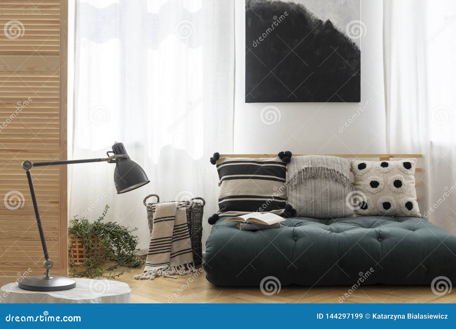 black and white painting above scandinavian futon with pillows in trendy living room interior, real photo with mockup on the empty