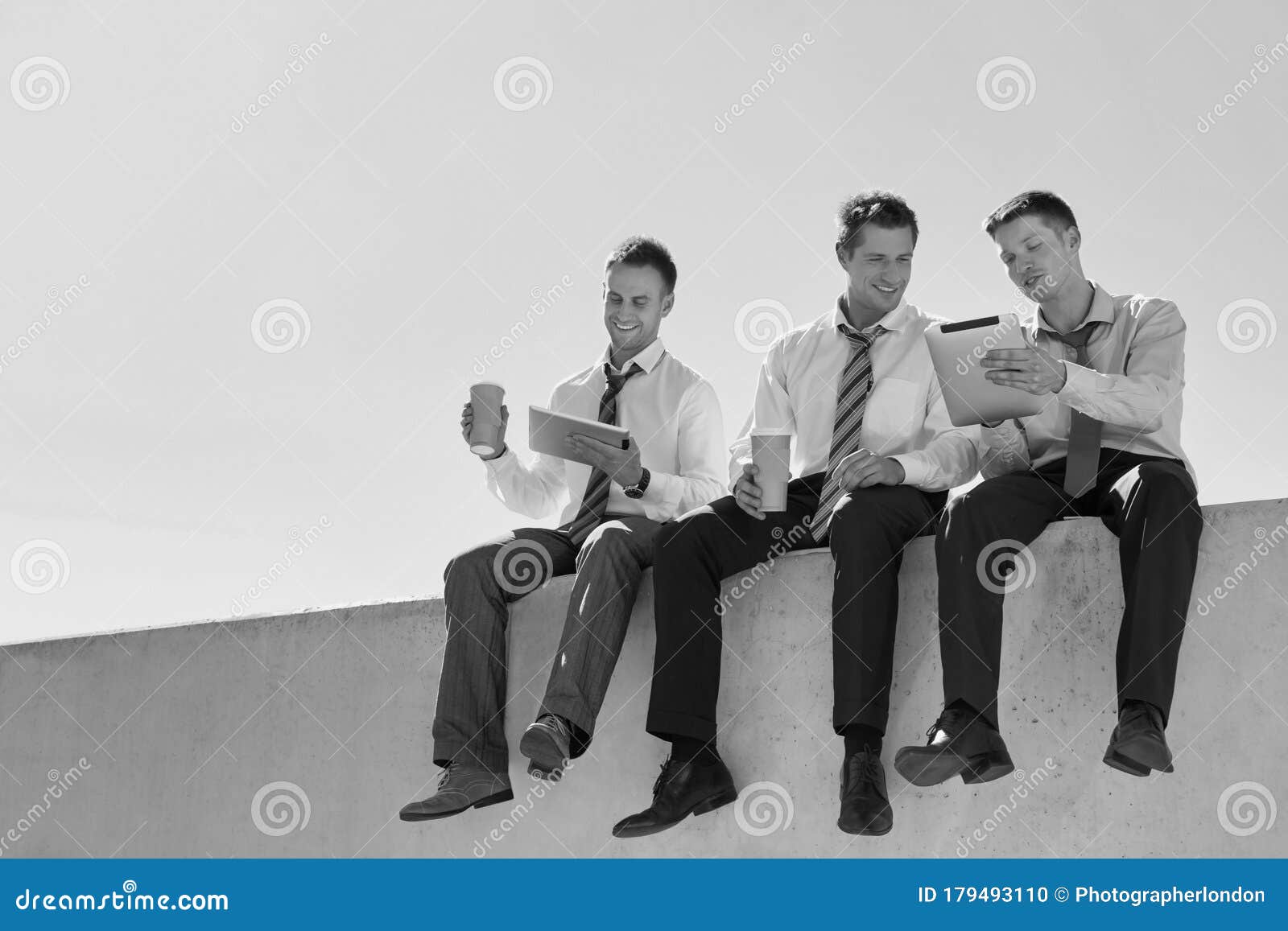 black and white photo of thoughtful businessmen sitting while using digita tablet in office rooftop