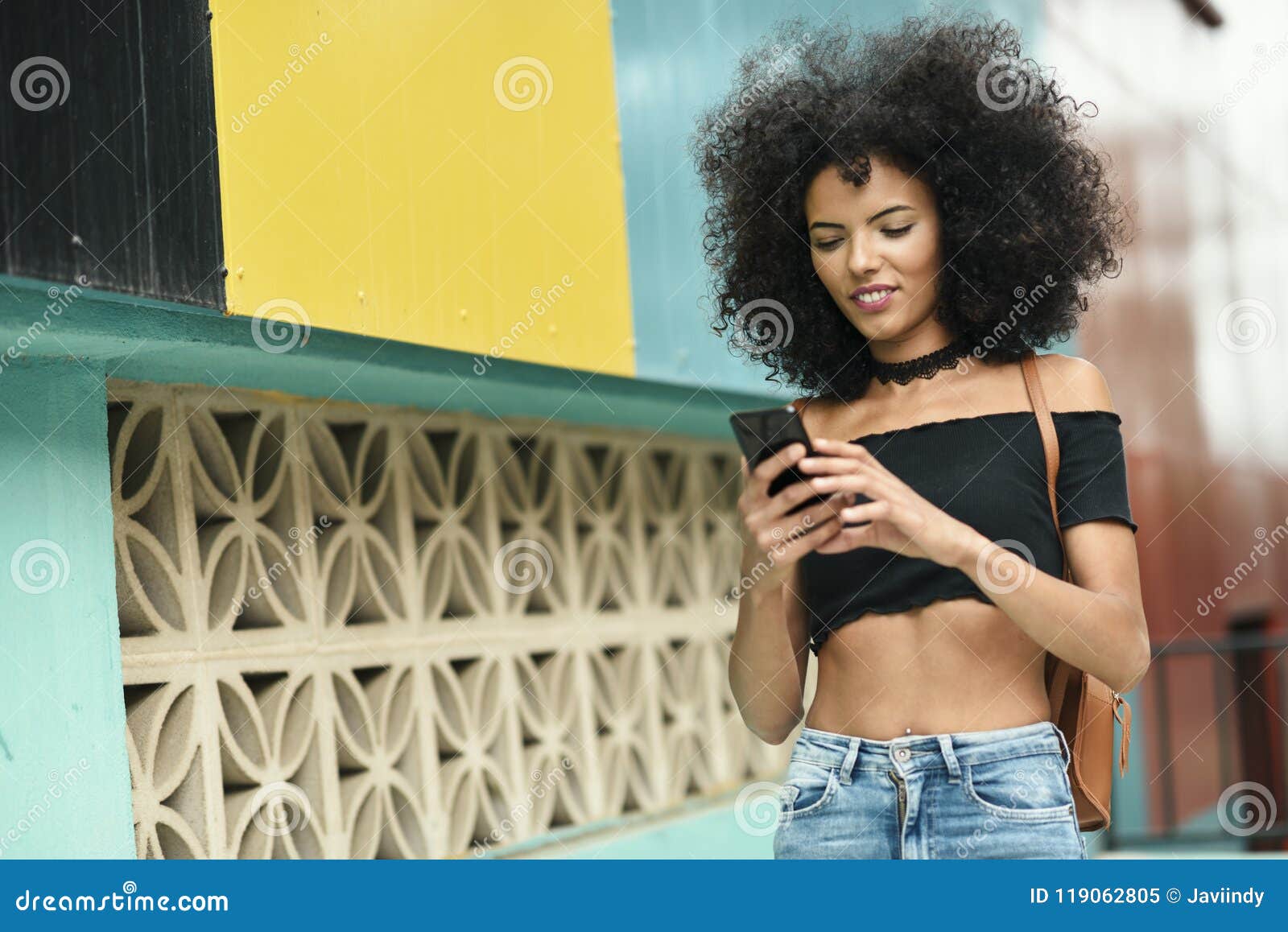 black woman afro hair on the street holding a smartphone