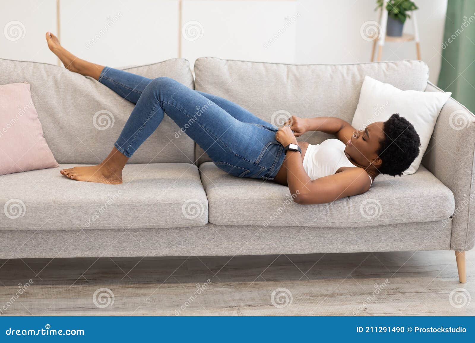 Black Woman Struggling Zipping Small Jeans Lying on Sofa Indoors Stock ...