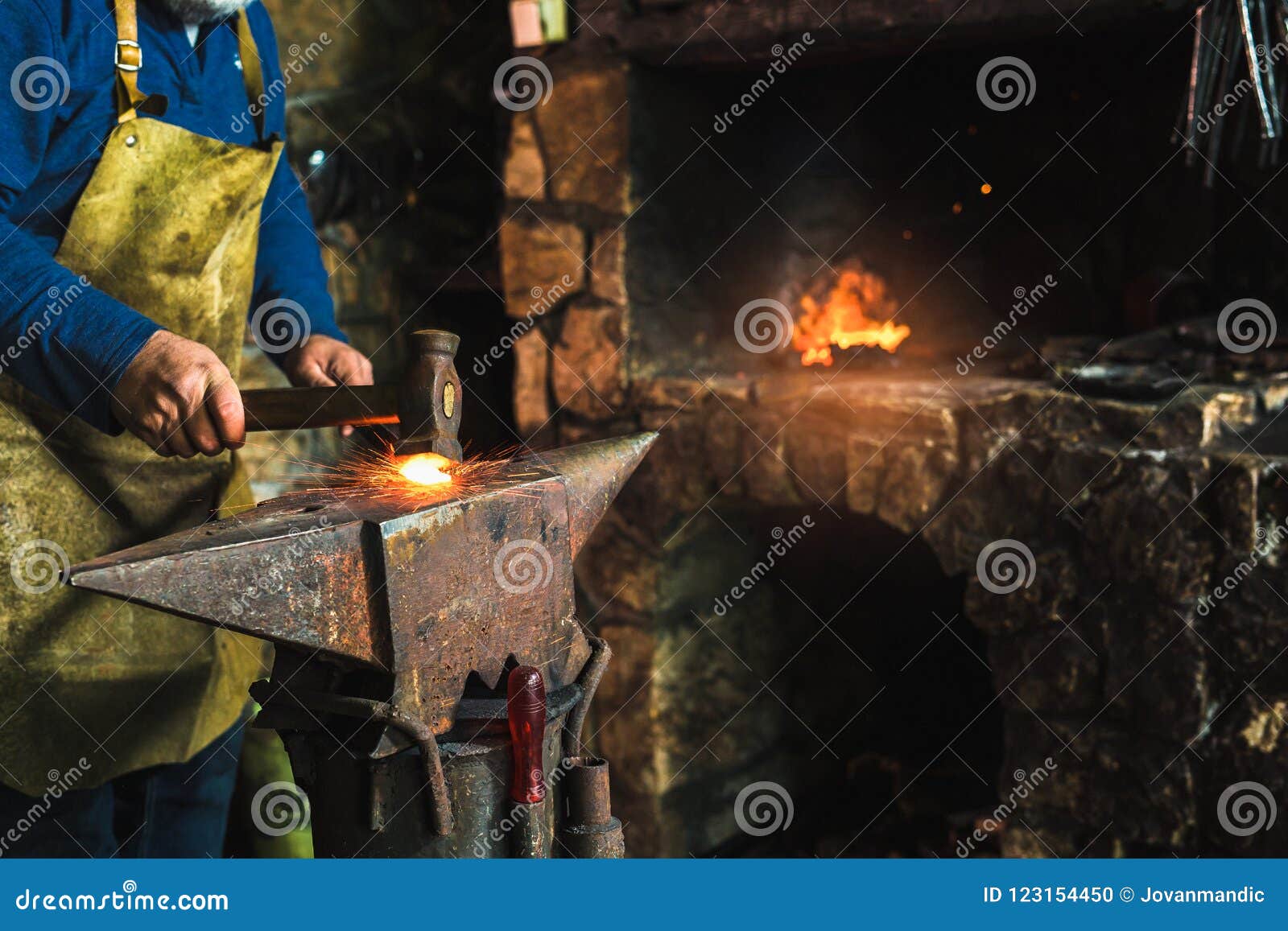 blacksmith manually forging the molten metal on the anvil in smithy