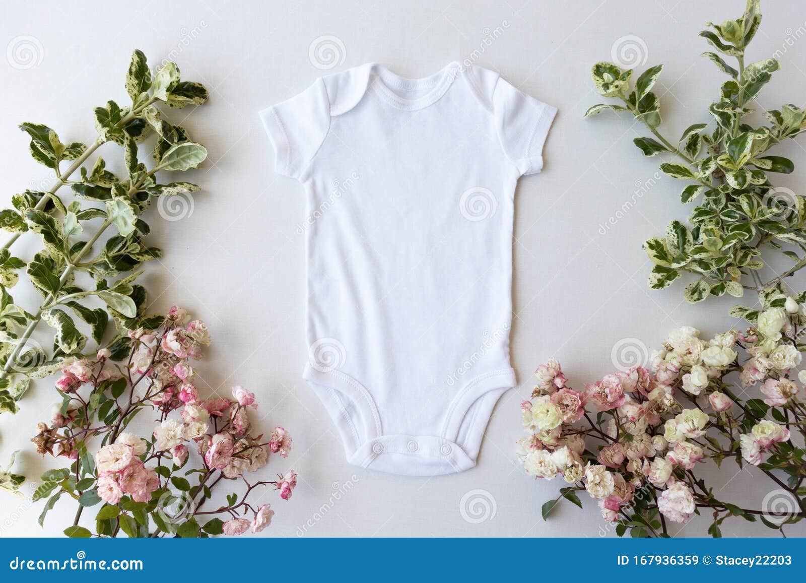 blank white baby grow on an off white background with green leaves and pink roses