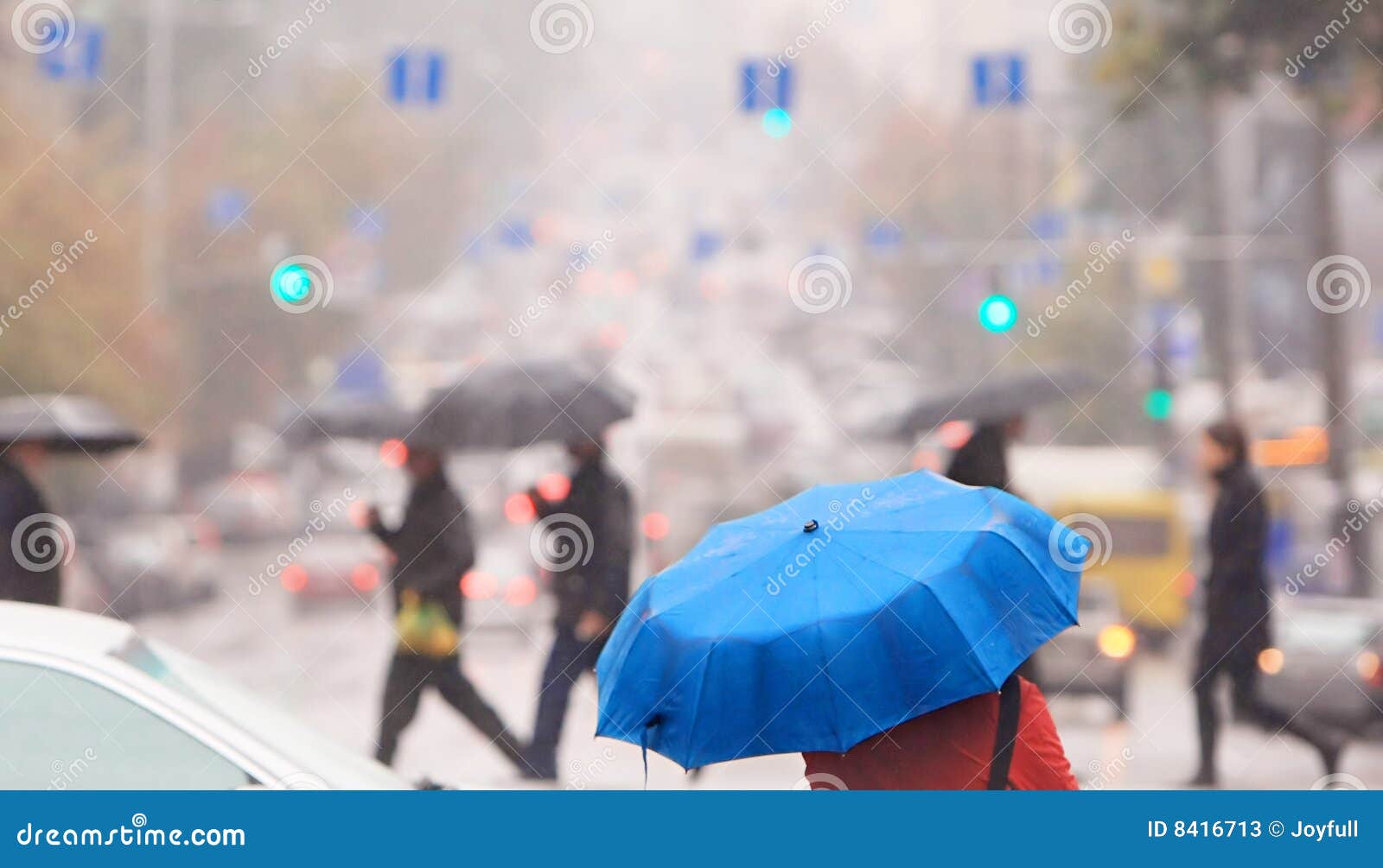 Blauer Regenschirm. Städtische Leute kreuzen die Straße im Regen