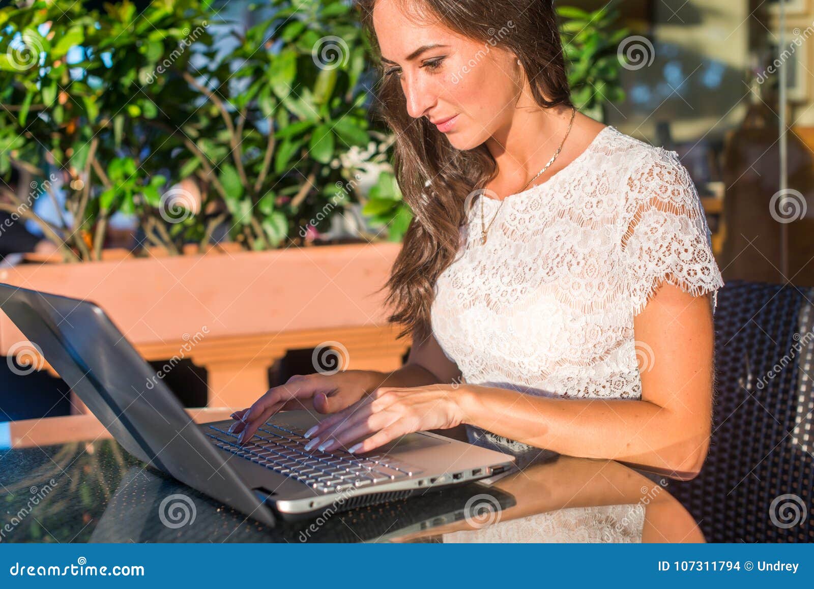 Blogger sorridente grazioso facendo uso del computer portatile per scrivere i blog mentre sedendosi al caffè all'aperto il giorno soleggiato
