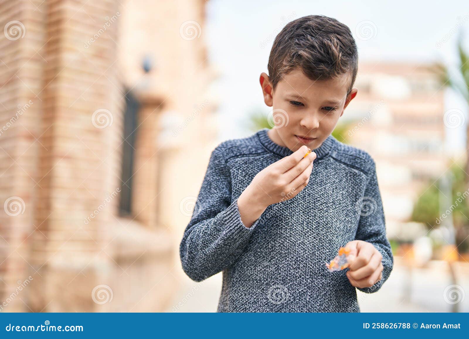 Blond Child Smiling Confident Eating Candy at Street Stock Photo