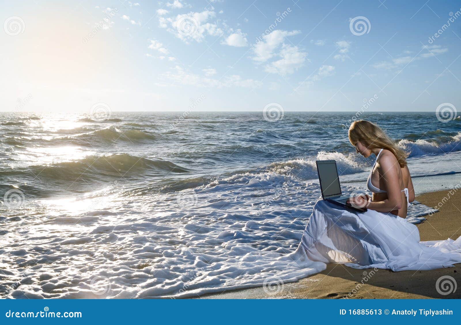 Blond girl using laptop on sea beach