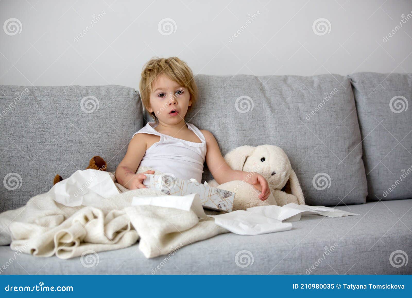 blond toddler child, wiping his nose in a tissue, sneezing and coughing