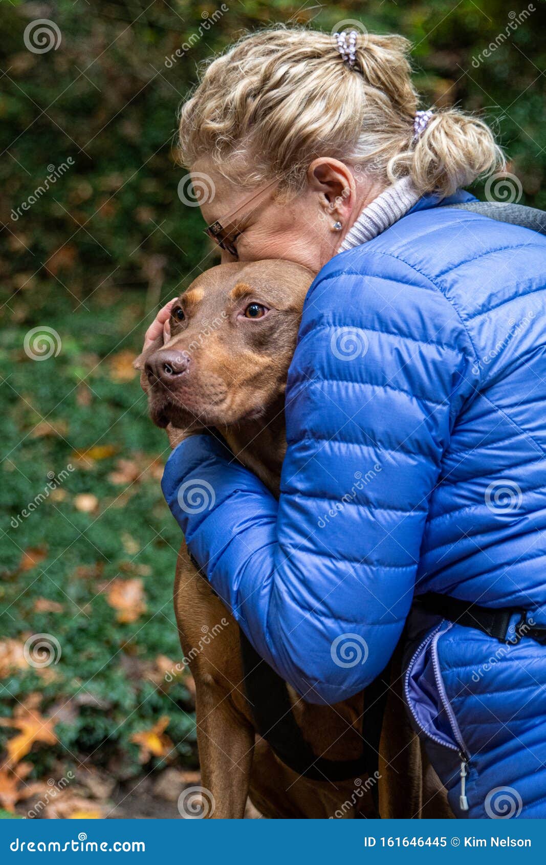blond woman hugging two toned brown doberman mix rescue dog, outside in nature