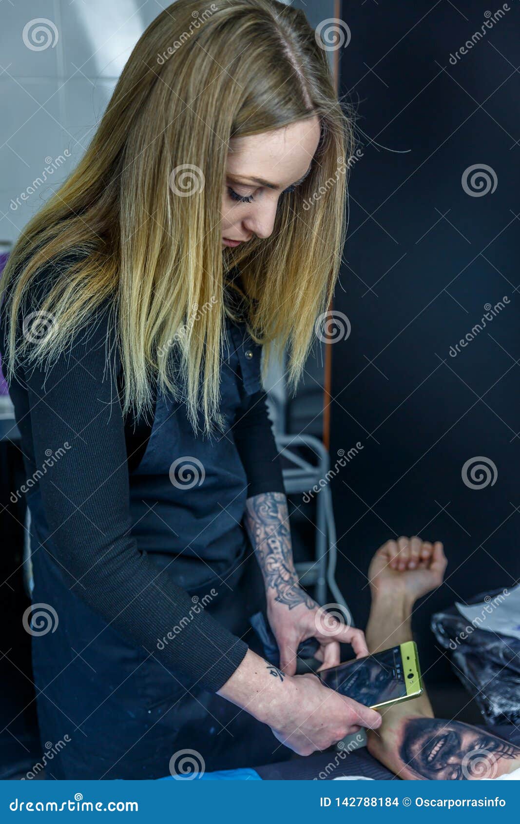 A Blonde Artist is Taking a Picture of the Tattoo she is Doing To Her ...