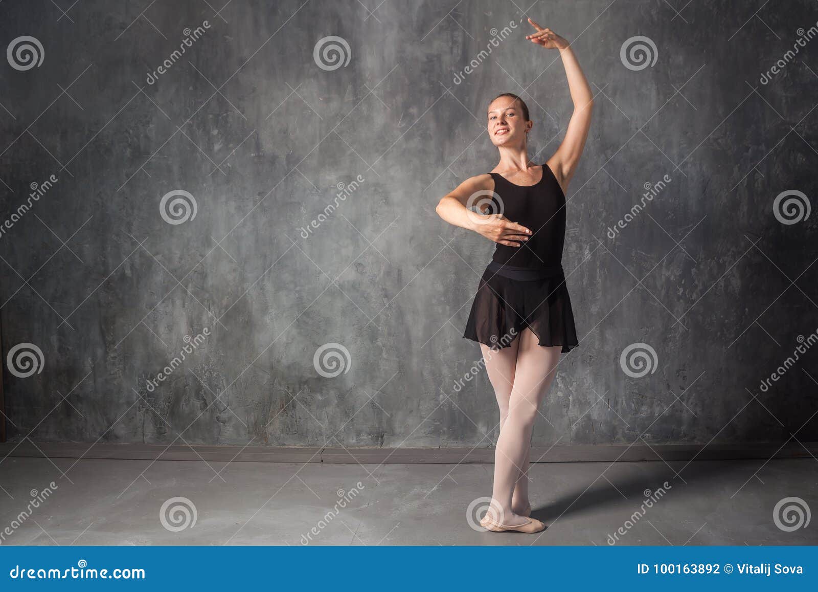 beautiful young blonde ballet dancer in a black dress, white pantyhose and  bouillant pointes dancing Russian ballet in a dark dance studio Stock Photo