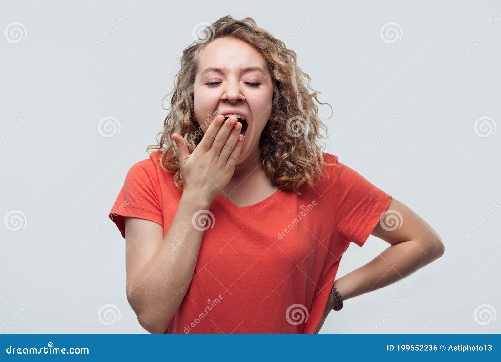 blonde girl bored and yawning tired covering mouth with hand. studio shot, white background. restless and sleepiness