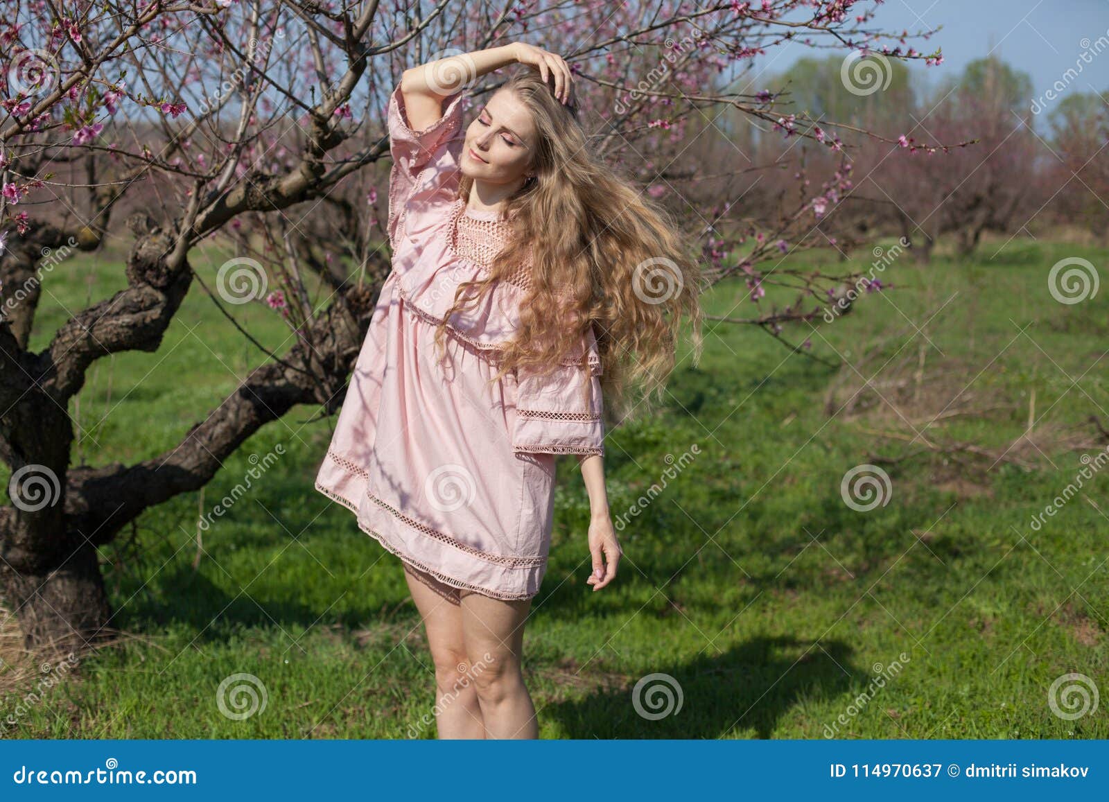 Blonde in pink dress walks in the garden with flowering trees 1