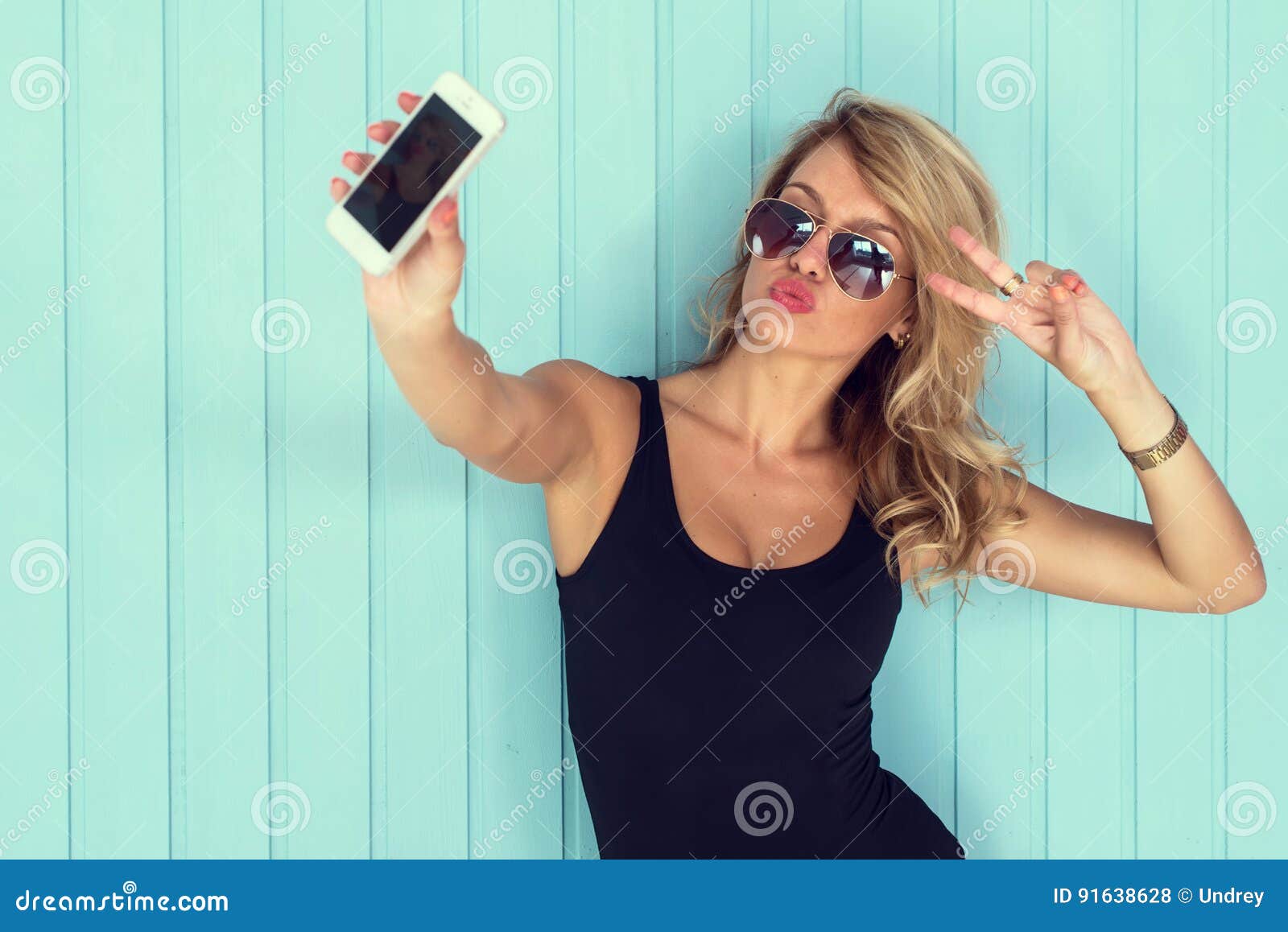 blonde woman in bodysuit with perfect body taking selfie smartphone toned instagram filter